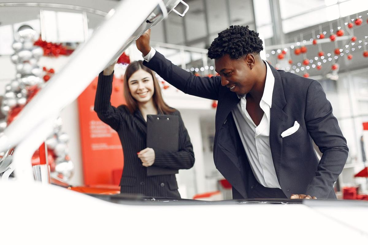 Homme et femme signant des papiers devant une voiture dans un salon de vente
