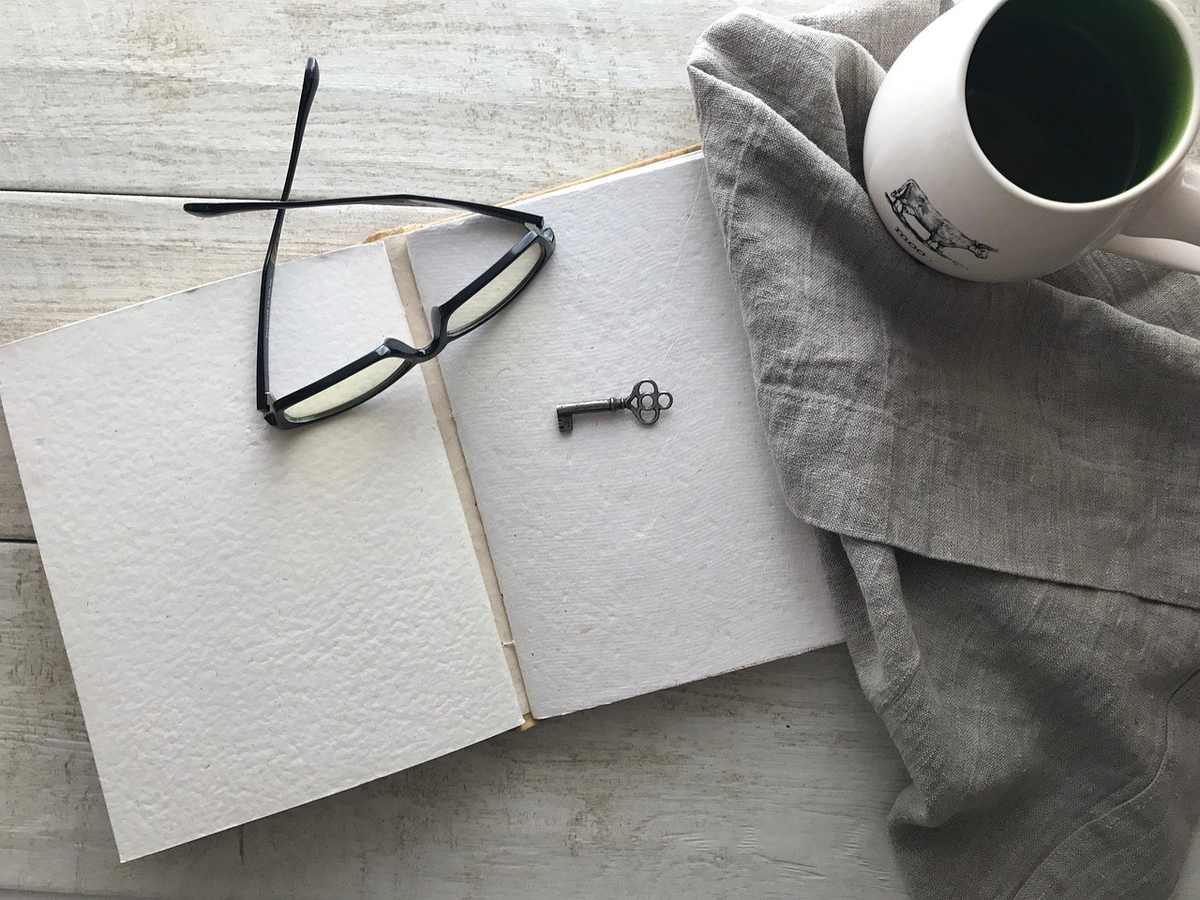 Carnet ouvert avec lunettes et clé, tasse de café sur tissu gris