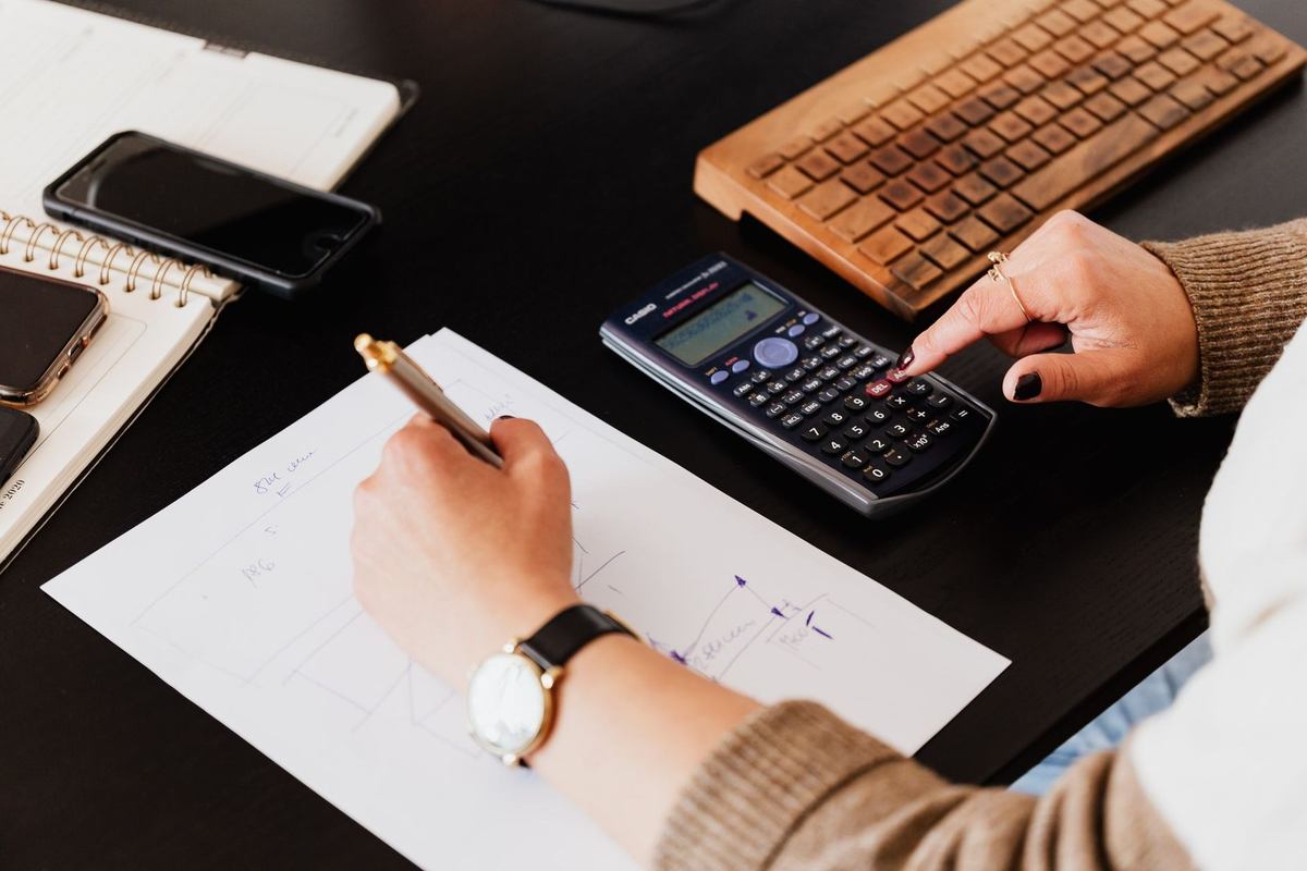 Une main écrit sur du papier avec une calculatrice et un smartphone à côté