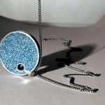 Pendentif rond bleu brillant attaché à une chaîne métallique sur fond clair