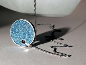 Pendentif rond bleu brillant attaché à une chaîne métallique sur fond clair
