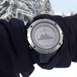 Montre connectée montrant une montagne sur son écran, portée sur un bras ganté