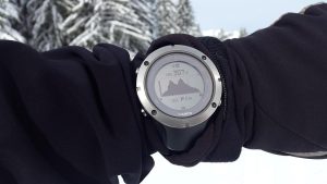 Montre connectée montrant une montagne sur son écran, portée sur un bras ganté