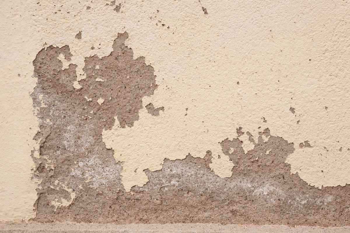 Enduit qui s'écaille sur un mur beige révélant la couche grise