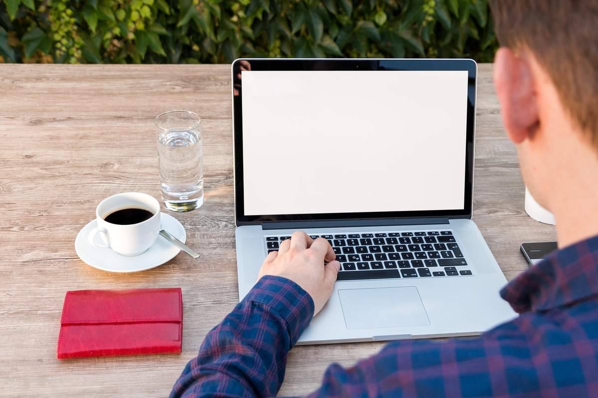 Une personne travaille sur ordinateur portable à l'extérieur avec café et verre